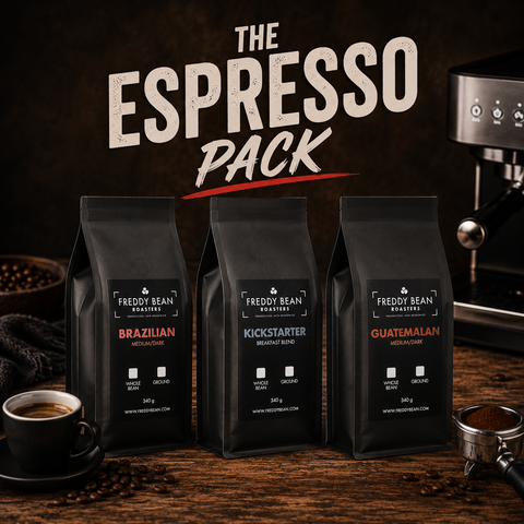 Three coffee bean bags from 'Freddy Bean Roasters' with an espresso machine and cup in the background.